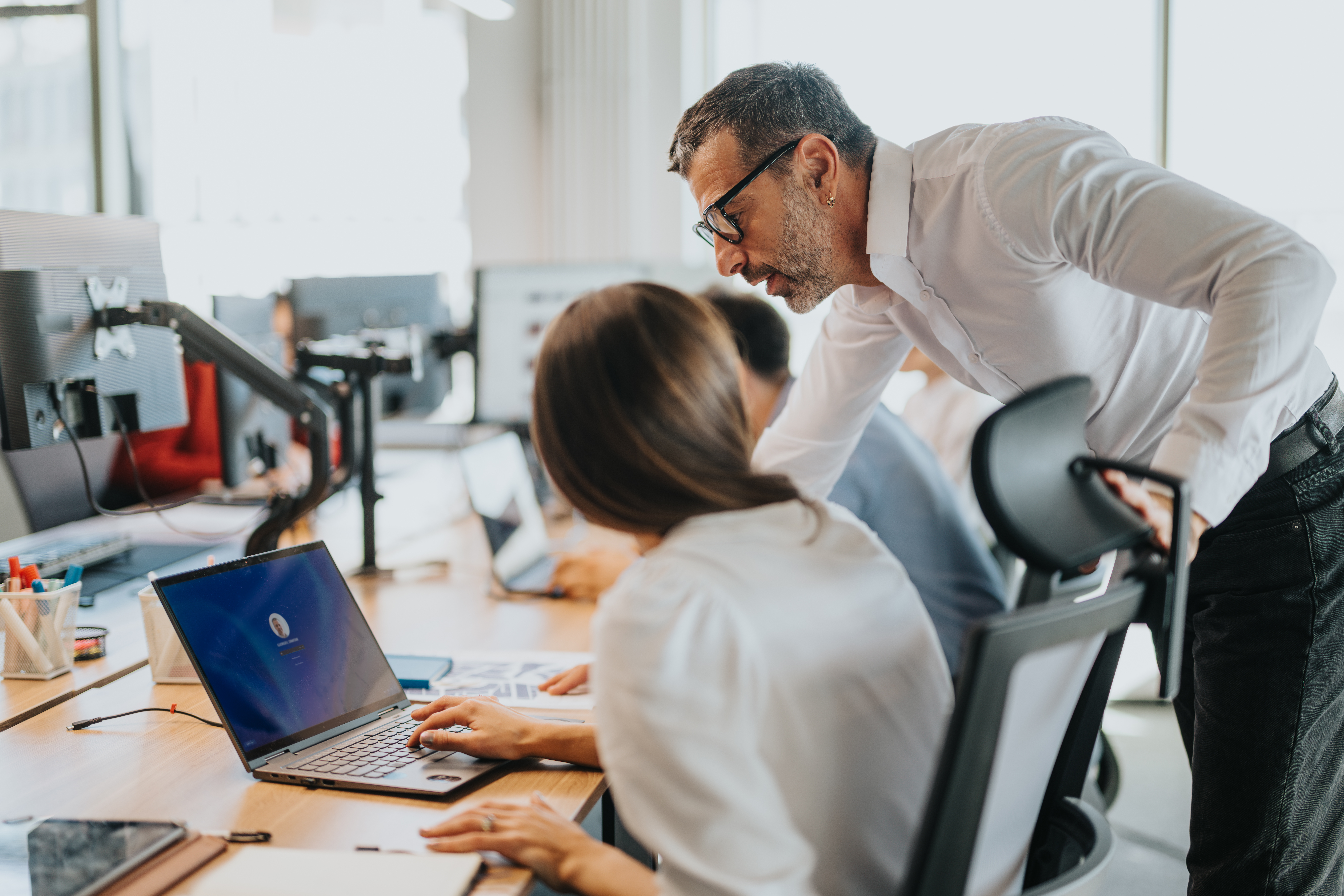 Business people working together in an open office space, focusing on teamwork and collaboration. A manager assists employees with tasks, fostering productivity and communication.