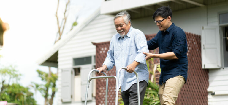 Elderly Asian father and Adult son walking in backyard. Positive Asian man caregiver helping patient