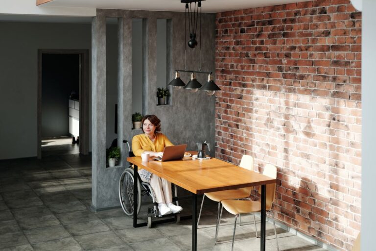 Modern office with a brick wall, featuring a woman in a wheelchair working on her laptop.