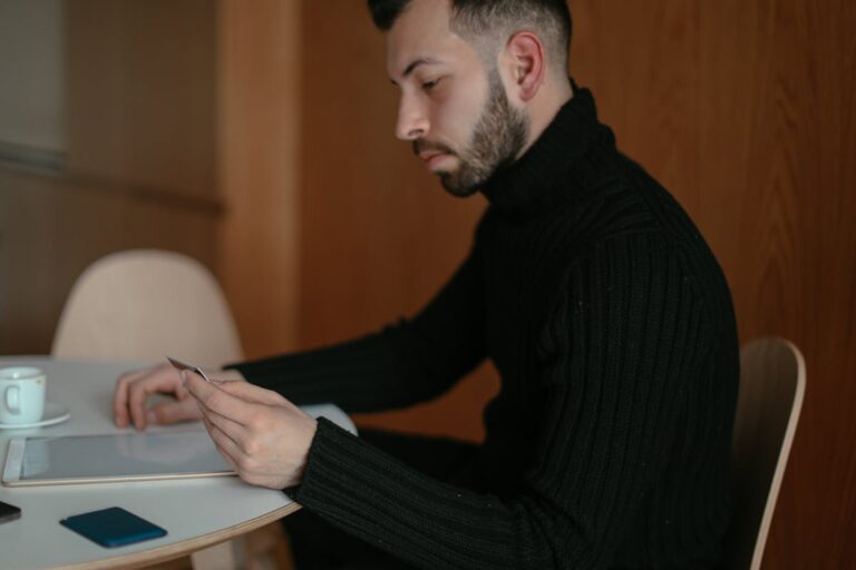Focused man in a black sweater uses a digital tablet at an indoor table, emphasizing technology and concentration.