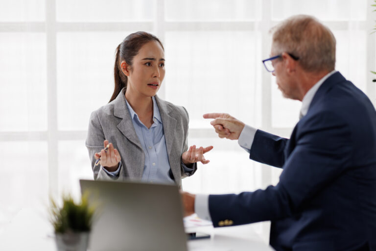 Asian businesswoman looking distressed and upset during a heated argument with an aggressive male manager pointing his finger, representing a tense workplace conflict, bullying, and power imbalance